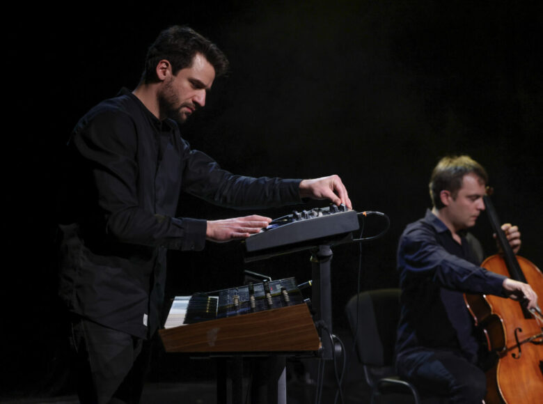 Na scenie mężczyzna grający na wiolonczeli oraz mężczyzna stojący przy syntezatorze dźwięku.