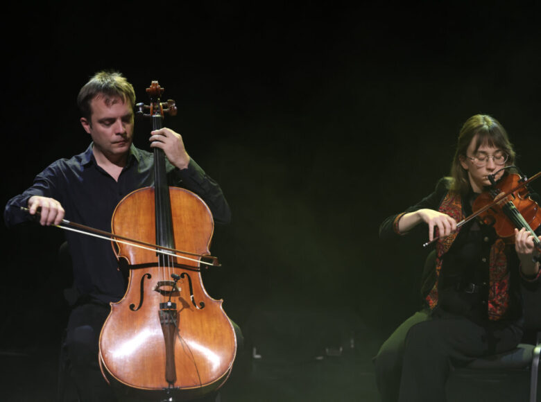 Na scenie na czarnym tle kobieta grająca na skrzypcach i mężczyzna grający na wiolonczeli.