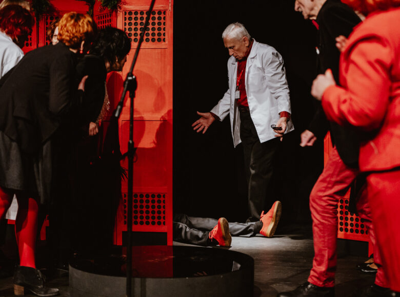Spektakl teatralny. Na ziemi leży mężczyzna. Pochyla się nad nim grupa osób.