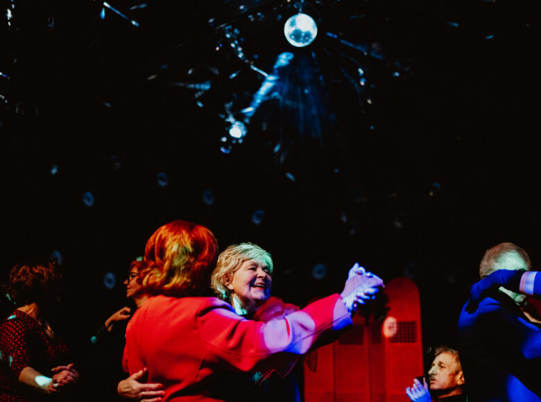 Ciemne pomieszczenie z punktowym oświetleniem. Grupa tańczących starszych osób.