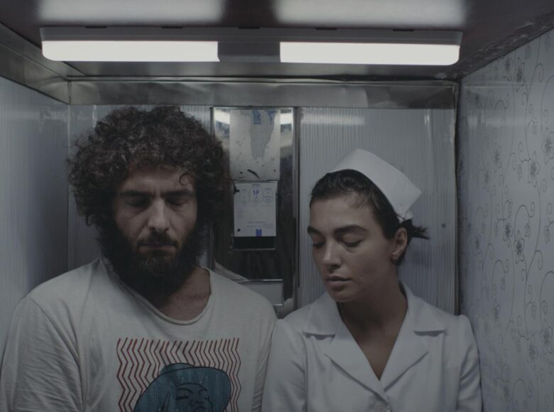 W malutkim, ciasnym i klaustrofobicznym pomieszczeniu stoją obok siebie kobieta w stroju pielęgniarki i mężczyzna.