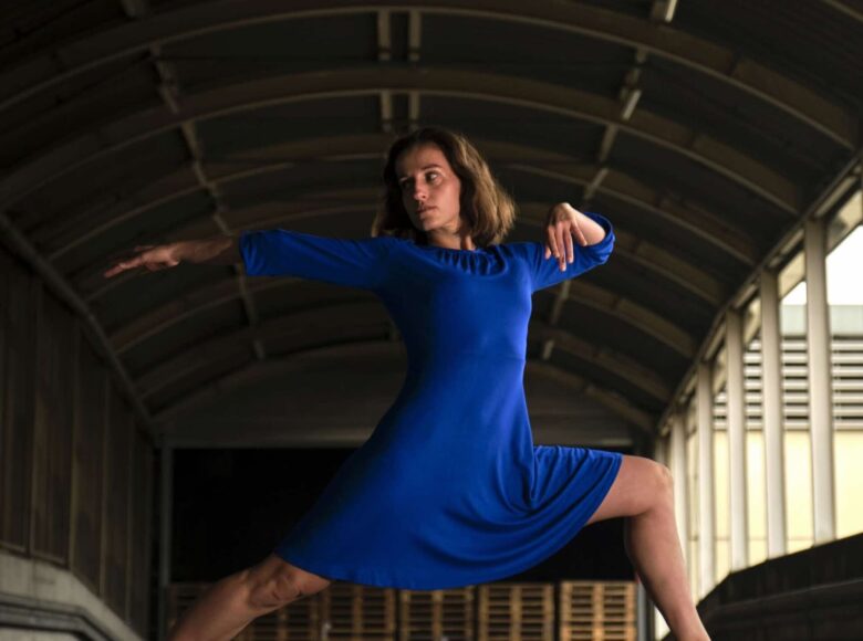 Tancerka tańca współczesnego tańczy w podcieniach jakiegoś budynku.