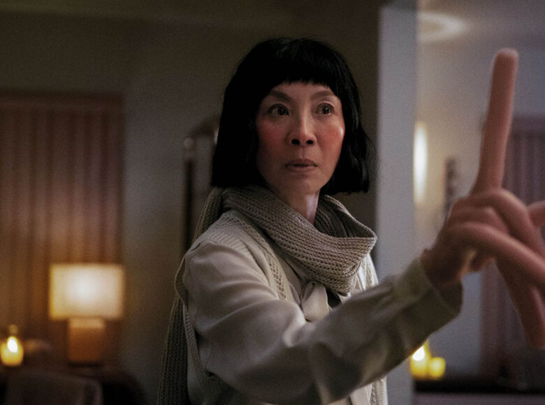 Wnętrze mieszkania. Na pierwszym planie kobieta. Zamiast dłoni ma protezę. Unosi do góry palec protezy skupiają na nim wzrok.