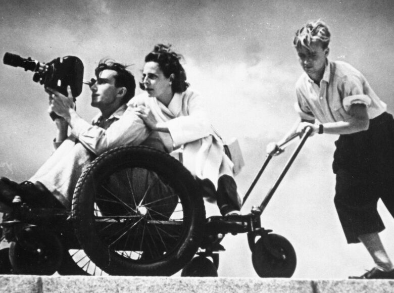 Fotografia czarno biała. Przedstawia reżyserkę Leni Riefenstahl z ekipą podczas kręcenia zdjęć do filmu "Olimpiada".