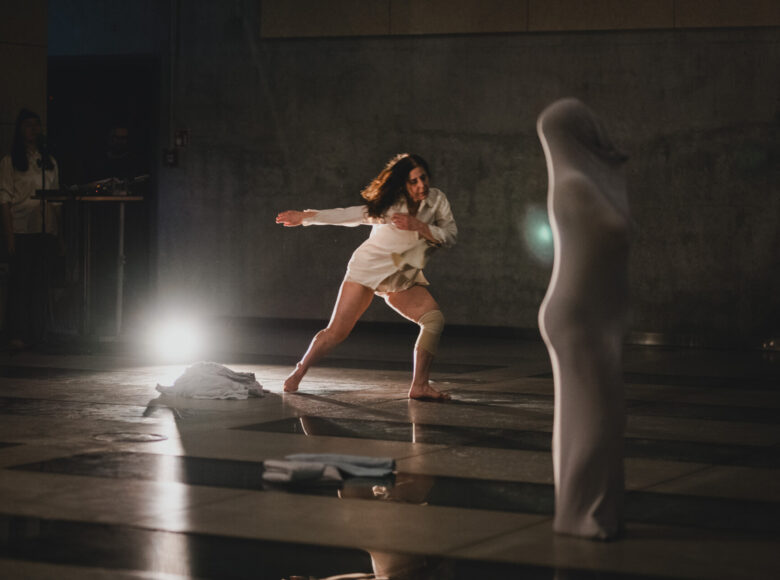 Spektakl tańca współczesnego. Na środku sceny tancerka w dynamicznej pozie. Obok stoi druga, spowita od ziemi do czubka głowy w elastyczną tkaninę, wygląda jak w kokonie. W głębi sceny stoją jeszcze dwie osoby.