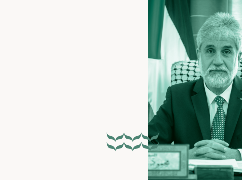 Portret mężczyzny w dojrzałym wieku. Mężczyzna jest siwy i brodaty. Ubrany jest w garnitur. Siedzi przy biurku.