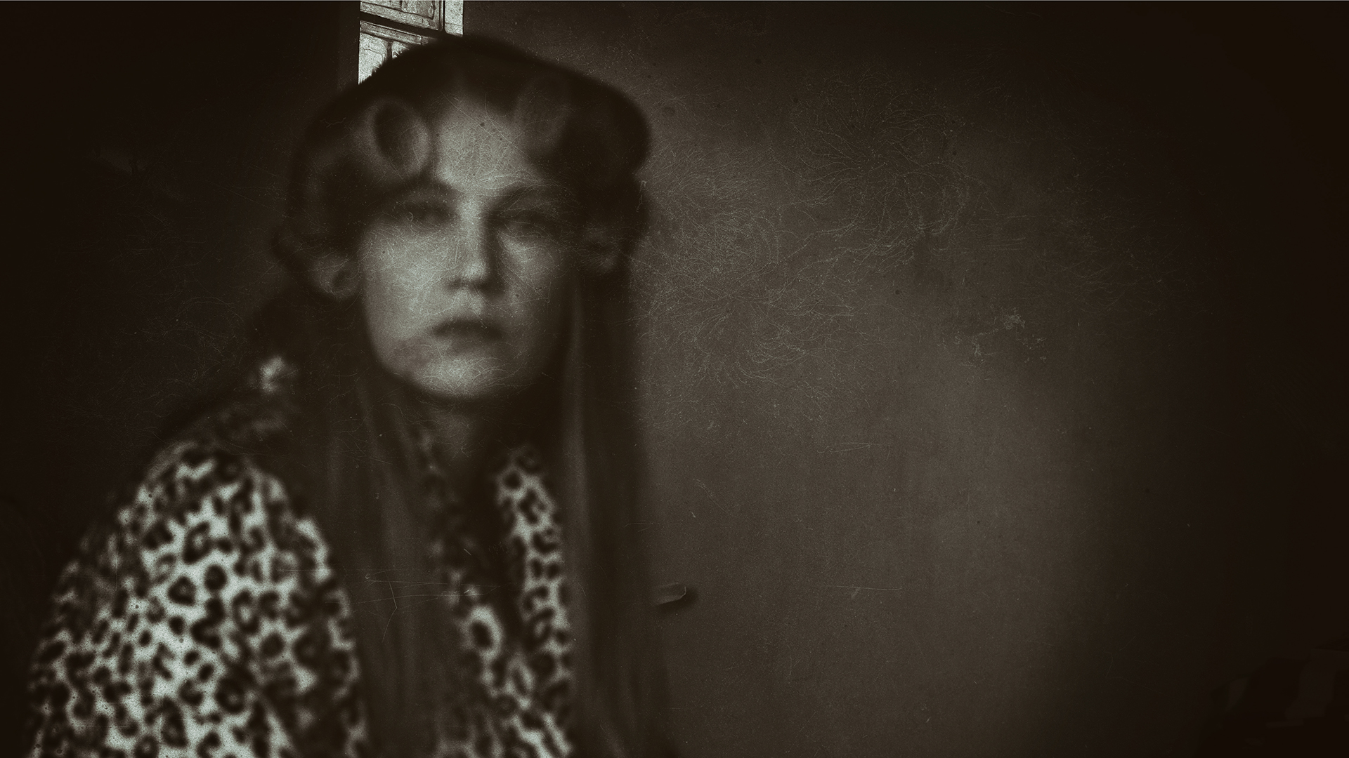 Czarno-biała fotografia, z odcieniami sepii, przedstawia portret młodej kobiety, z długimi ciemno bląd włosami, zakręconymi po obydwu stronach czoła w dwa grube loki.