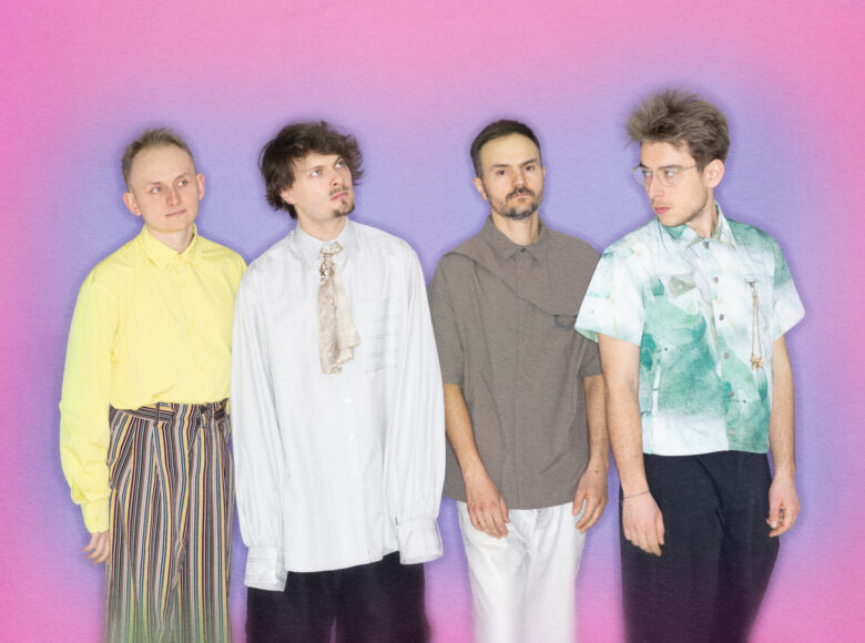 Czterej młodzi mężczyźni stoją na tle kolorowej ściany pozując do fotografii.