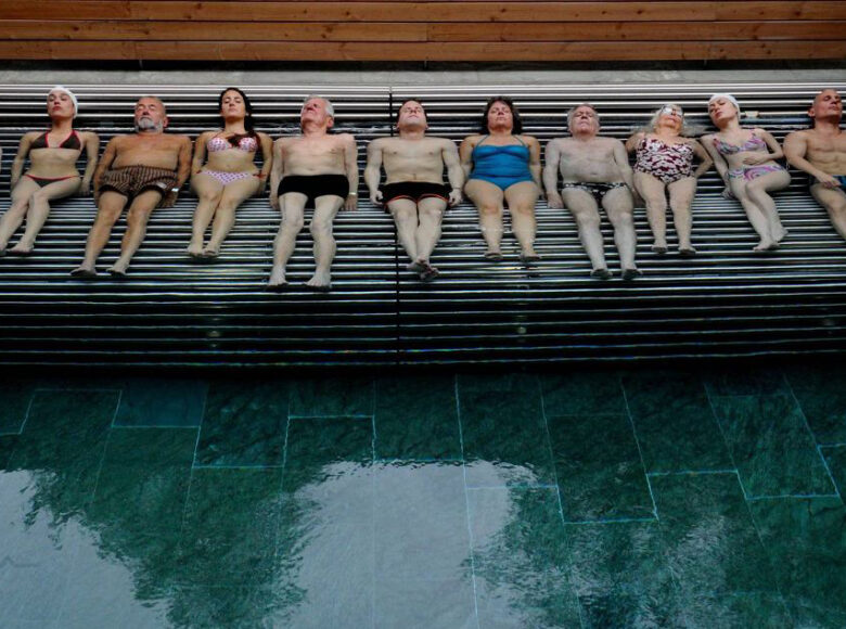 Osoby w kostiumach kąpielowych leżą jedna obok drugiej na brzegu basenu kąpielowego.