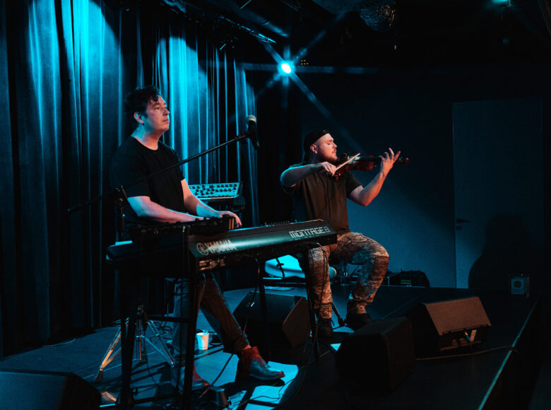 Koncert muzyki współczesnej. Na scenie dwóch muzyków. Jeden gra na klawiszach, drugi na skrzypcach.