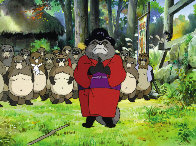 Kadr z filmu animowanego. Na trawie wśród drzew stoi-pracz szop ubrany w kimono. Za nim grupa innych szopów. W tle chata kryta strzechą.