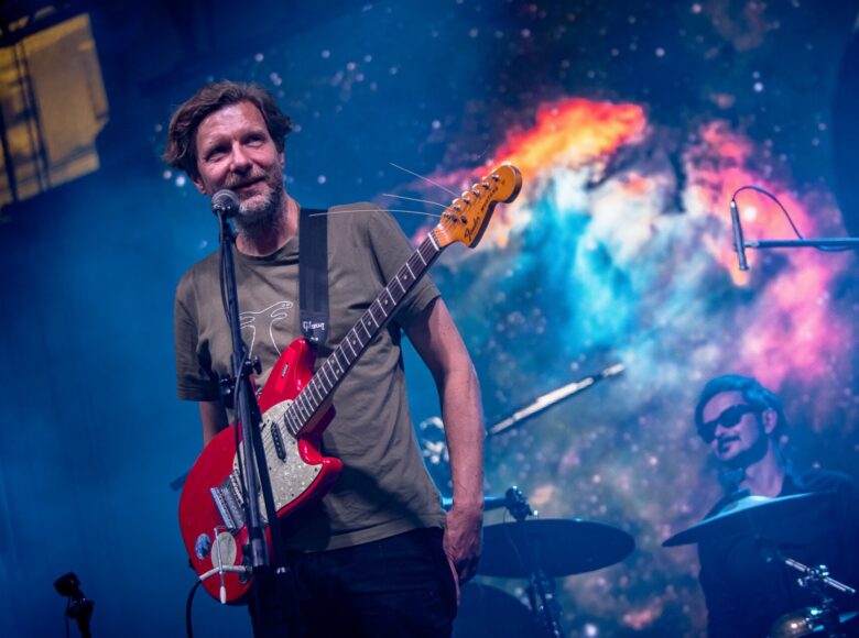 Koncert muzyki współczesnej. Na scenie muzyk z gitarą elektryczną oraz perkusista.