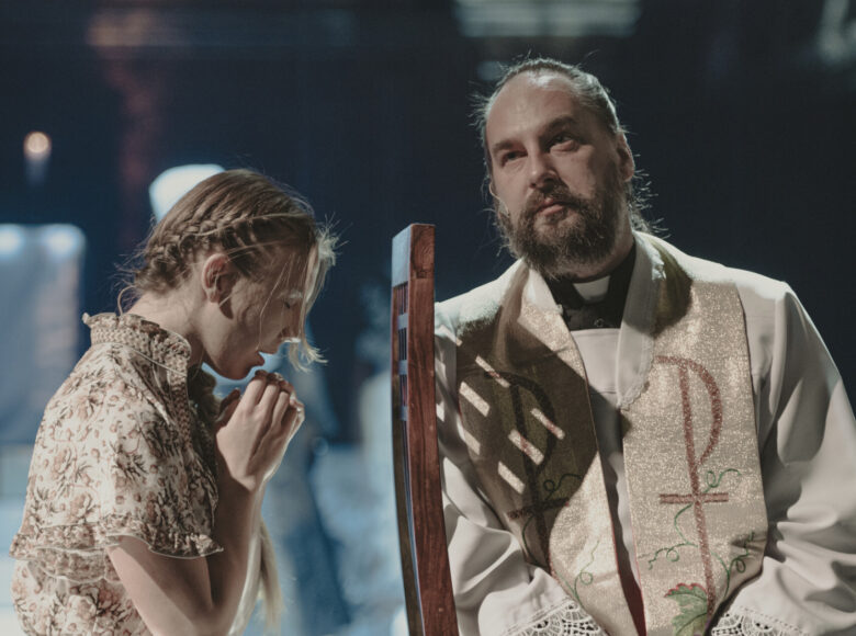 Spektakl teatralny. Aktorka w letniej sukience i aktor w sutannie odgrywają scenę spowiedzi.