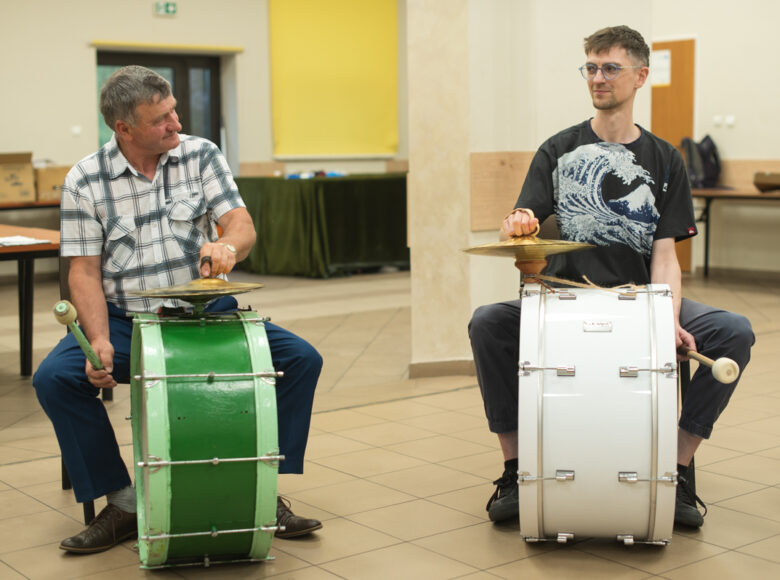 W pomieszczeniu dwóch mężczyzn gra na bębnach.