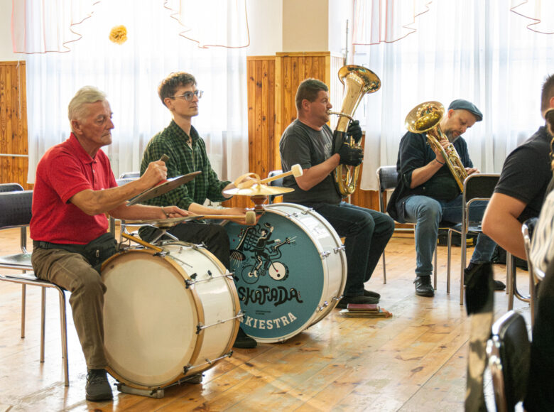 W dużej sali grupa mężczyzn grających na instrumentach dętych i perkusyjnych.