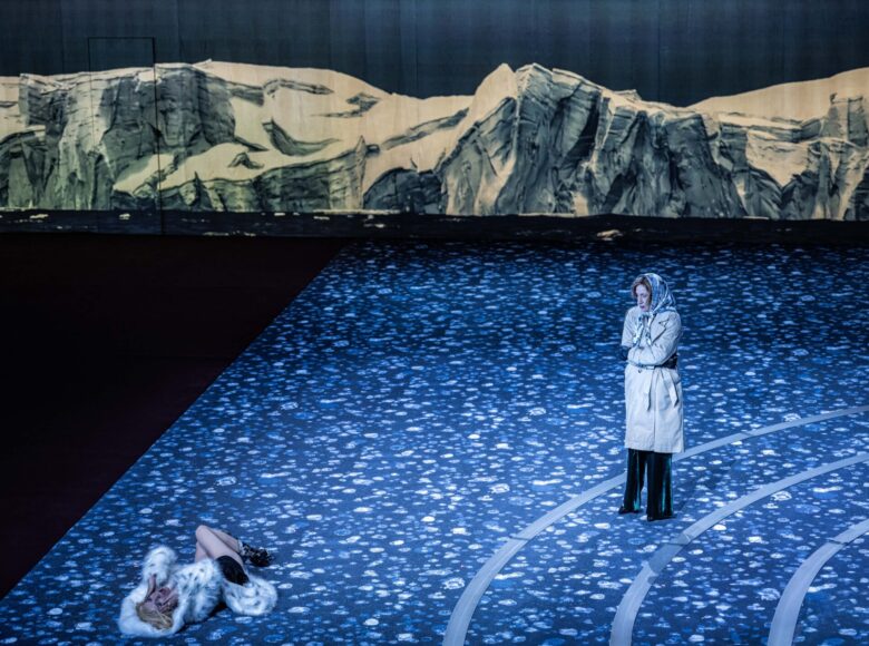 Na scenie dwie kobiety .Jedna, w płaszczu i chustce na głowie, stoi w milczeniu. Druga, w białym futrze, leży i krzyczy. W tle za nimi dekoracja przedstawiająca skały.