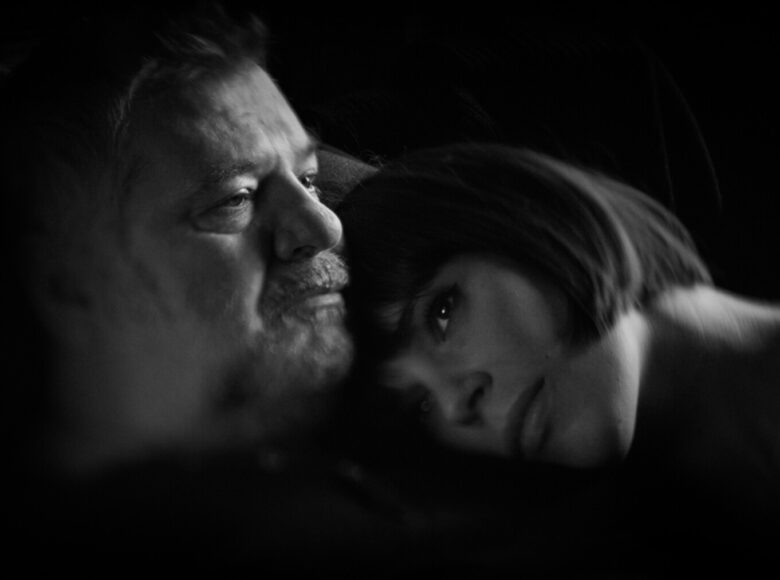 Fotos czarno biały z filmu. Zbliżenie na twarze kobiety i mężczyzny w półmroku. Kobieta kładzie mężczyźnie głowę na ramieniu. Za nimi czarne tlo