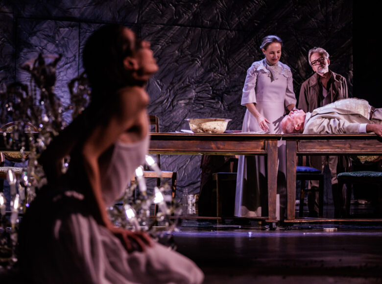 Spektakl teatralny. Na pierwszym planie kobieta odchylona do tyłu. W głębi przy stole stoi kobieta z mężczyzną. Patrzą na leżącego na stole mężczyznę. Obok leżącego mężczyzny stoi emaliowa, przybrudzona miska.