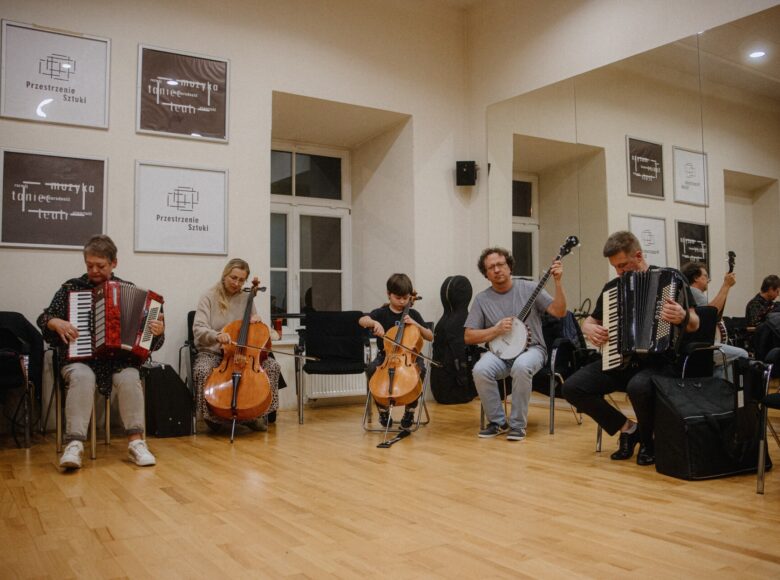 W sali kilka kobiet, mężczyzn i chłopiec, grający na akordeonach, wiolonczelach i na banjo.