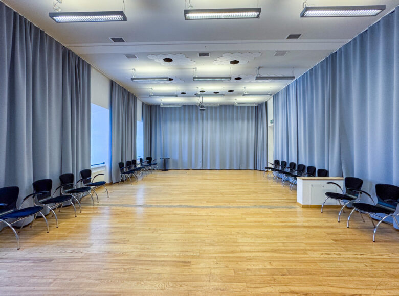 Wnętrze przestronnej sali - tak zwanej "sali jasnej" w Centrum Kultury w Lublinie. W sali kilkanaście krzeseł ustawionych w rzędy pod ścianami. Ściany zasłonięte kotarami.