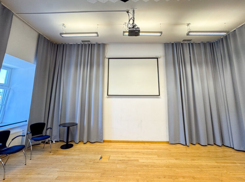 Wnętrze sali - tak zwanej "sali jasnej" w Centrum Kultury w Lublinie. W sali krzesła pod oknem oraz ekran na ścianie. Przy oknie i przy ścianie kotary.