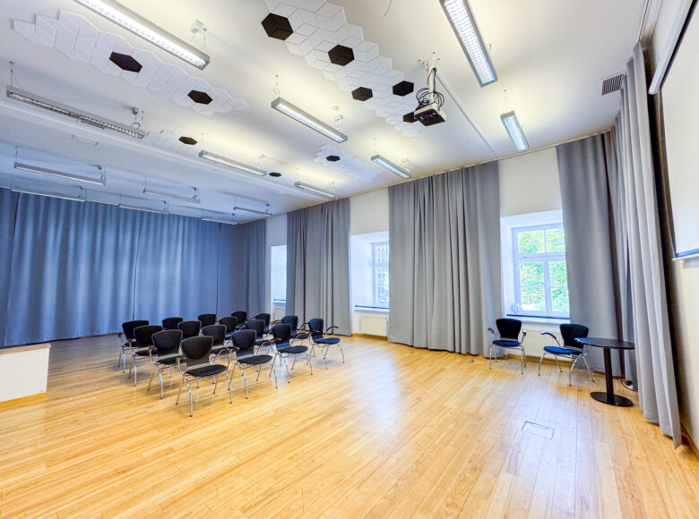 Wnętrze przestronnej, jasnej sali - tak zwanej "sali jasnej" w Centrum Kultury w Lublinie. W sali kilkanaście krzeseł ustawionych w rzędy, a przy oknach i na ścianach kotary.