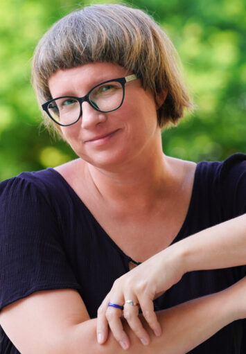 Fotograficzny portret młodej kobiety na tle zielonych drzew.