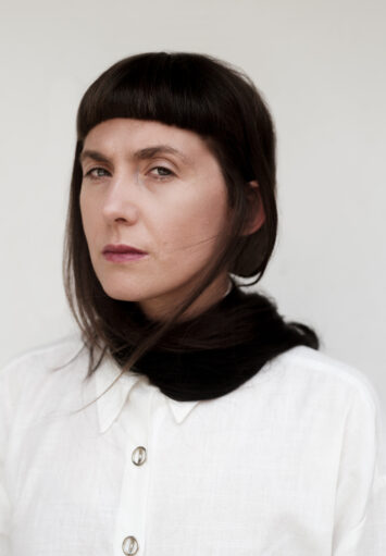 Fotograficzny portret kobiety w średnim wieku. Kobieta nosi białą bluzkę i pozuje na białym tle.