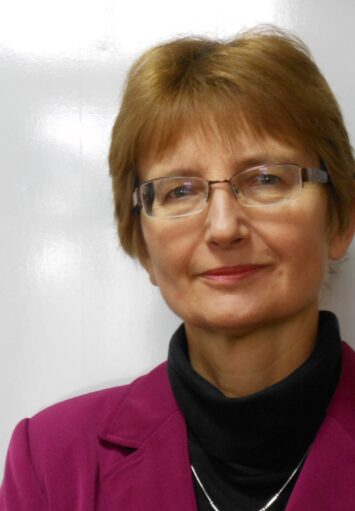 Fotograficzny portret kobiety w średnim wieku na neutralnym, szarym tle.