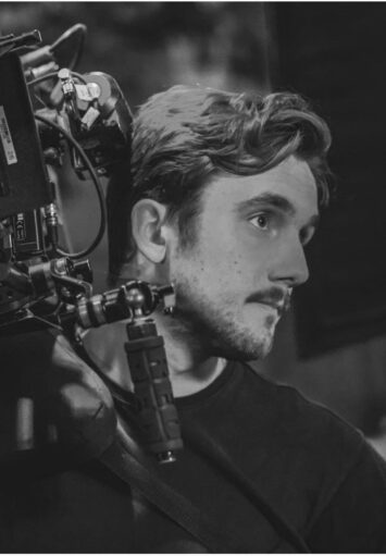 Zbliżenie na twarz i ręce mężczyzny trzymającego na ramieniu kamerę filmową.