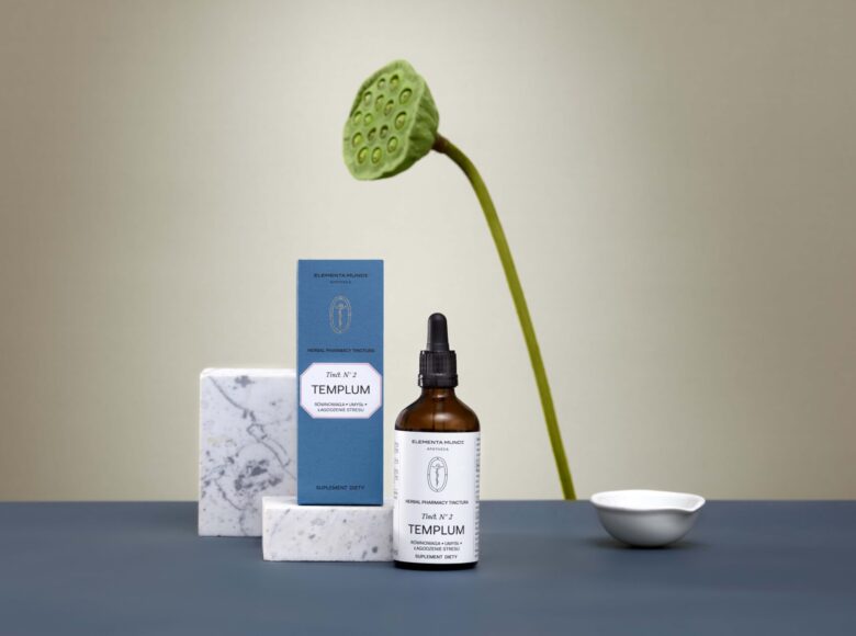 Na żółtym tle ustawione pudełeczko i flakonik z kosmetykami oraz kwiat.