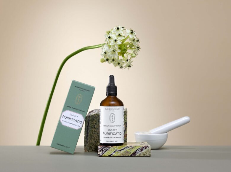 Na jasnym tle ustawione pudełeczka i flakonik z kosmetykami oraz kwiat.