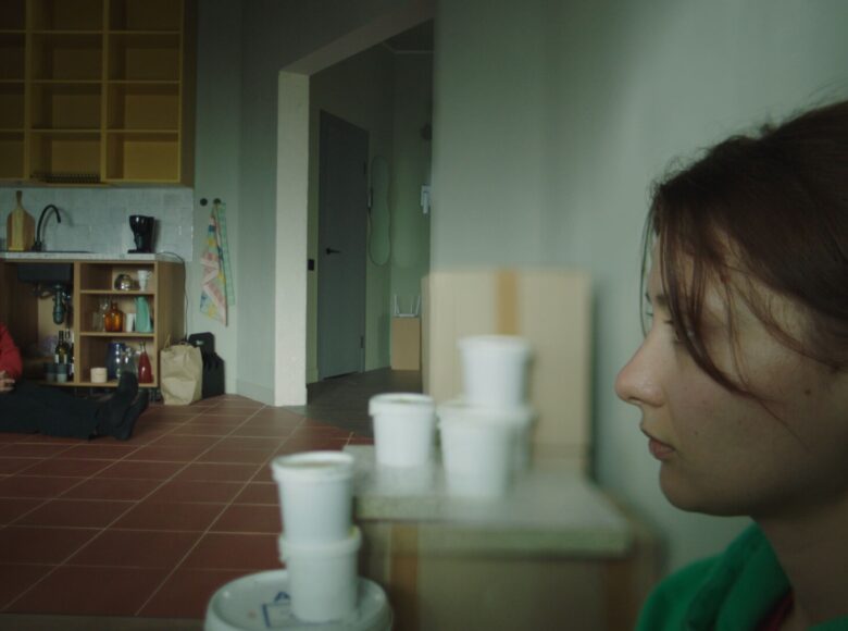 Kadr z filmu. Kuchnia w mieszkaniu, Na pierwszym panie zbliżenie na profil młodej kobiety, patrzącej przed siebie. W tle pod kuchennymi szafkami na podłodze siedzi młody mężczyzna.