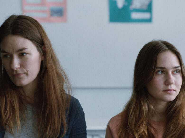 Kadr z filmu. W pomieszczeniu na pierwszym planie kobieta i młoda dziewczyna. Stoją obok siebie, ale każda z nich patrzy w inną stronę.