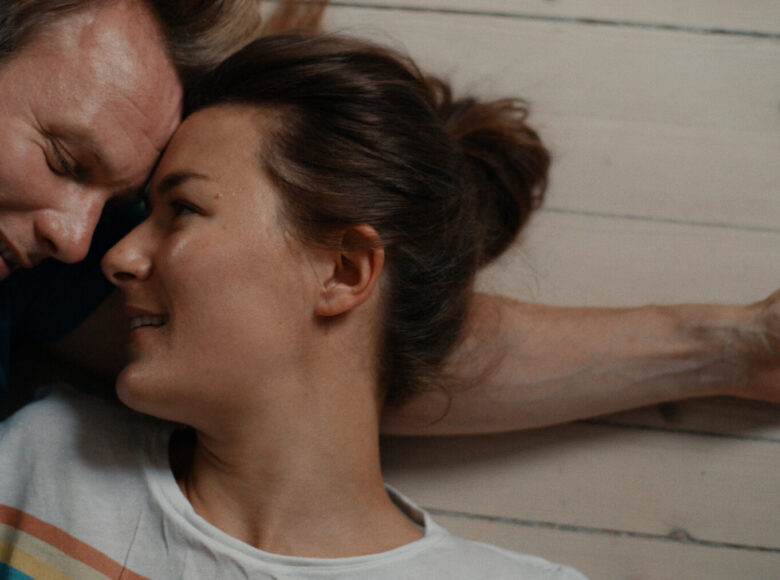 Kadr z filmu. Zbliżenie na twarze i ramiona dziewczyny i chłopaka, przytulających się do siebie.