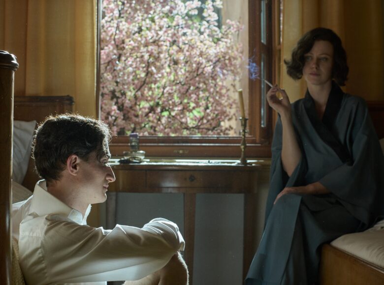 Kadr z filmu. W pokoju obok siebie stoją dwa łóżka. Na jednym z nich siedzi młoda kobieta z papierosem, ubrana w szlafrok. Na podłodze przy drugim łóżku siedzi młody mężczyzna w koszuli, bez spodni. Za nimi okno, za którym widać kwitnące drzewo owocowe.