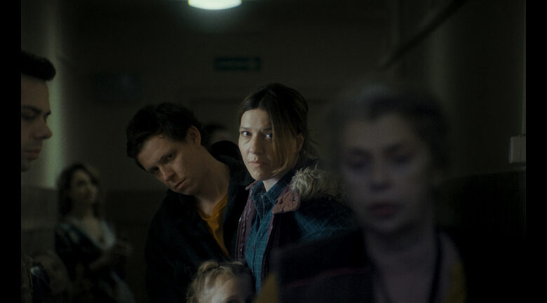 Kadr z filmu. W korytarzu w budynku użyteczności publicznej cztery dorosłe osoby i dziecko. Wyglądają na zmęczonych.