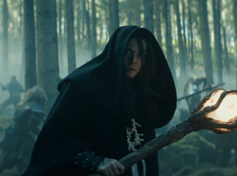 Kadr z filmu fantasy. Na pierwszym planie długowłosy mężczyzna w pelerynie z kapturem. W ręku ma konar drzewa z przymocowaną na końcu świecącą bryłą. W tle las i inni mężczyźni, walczący ze sobą.