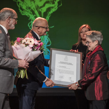Uroczystość na scenie. Anna Nawrot, założycielka Galerii Białej w Lublinie, otrzymuje dyplom od prezydenta Lublina, Krzysztofa Żuka. Obok stoi zastępczyni prezydenta Beata Stepaniuk-Kuśmierzak oraz lubelski radny Jarosław Pakuła, który trzyma w rękach bukiet kwiatów.