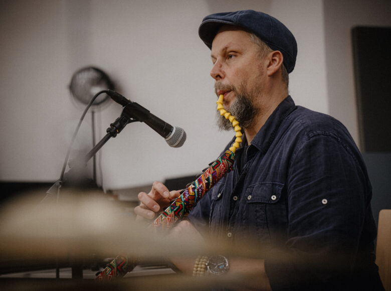 W pomieszczeniu przed mikrofonem siedzi mężczyzna grający na melodyce - dętym instrumencie muzycznym z klawiszami.