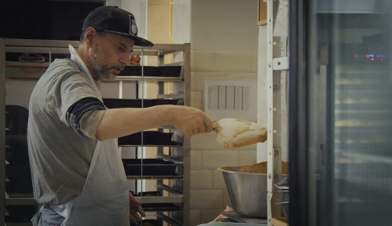 Kadr z filmu. Wnętrze piekarni. Mężczyzna w kucharskim fartuchu pracuje nad wyrobem pieczywa.