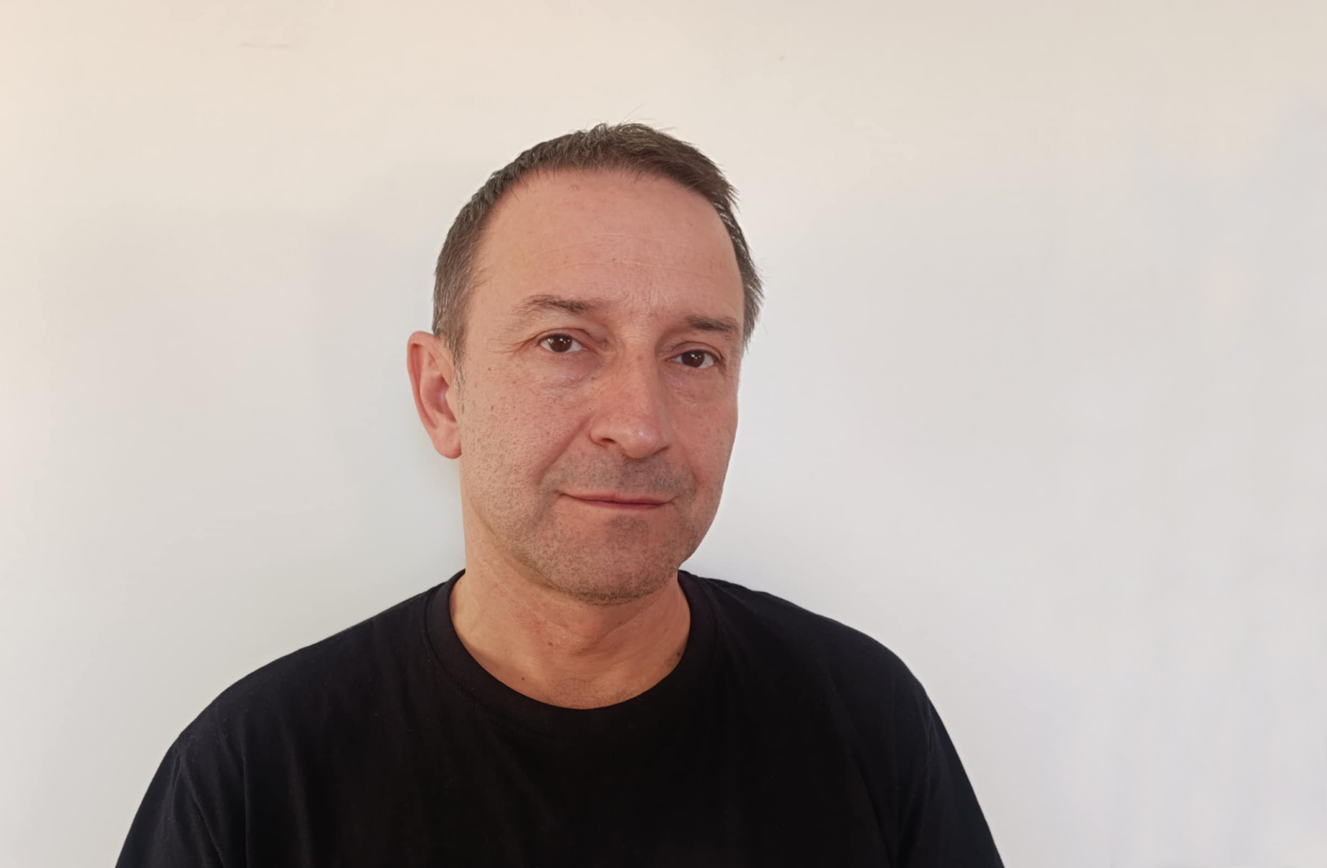 Na czarno-białej fotografii widzimy młodego mężczyznę, z krótkimi ciemnymi włosami, ubranego w czarną podkoszulkę.