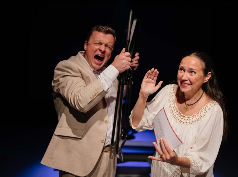 Spektakl teatralny. Na scenie kobieta i krzyczący coś do niej mężczyzna. Za nimi czarne tło.