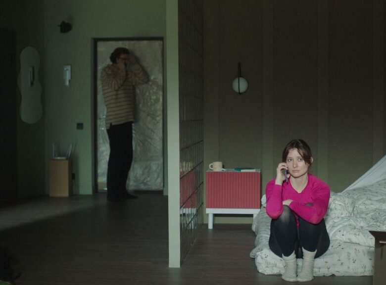 Kadr z filmu. W mieszkaniu pomieszczenie przedzielone ścianką. Z jednej strony ścianki, pod drzwiami wejściowymi do mieszkania stoi mężczyzna mówiący do telefonu komórkowego. Z drugiej strony ścianki, na łóżku siedzi młoda dziewczyna z telefonem komórkowym przy uchu i słucha.