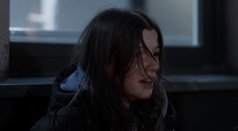 Kadr z filmu. Zbliżenie na twarz dziewczyny w zimowej kurtce, siedzącej na tle okna.