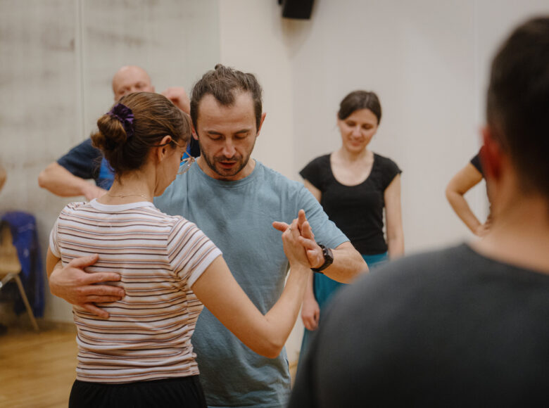 W pomieszczeniu tańcząca para. Dookoła stoi kilka osób, przyglądających się tańczącym.