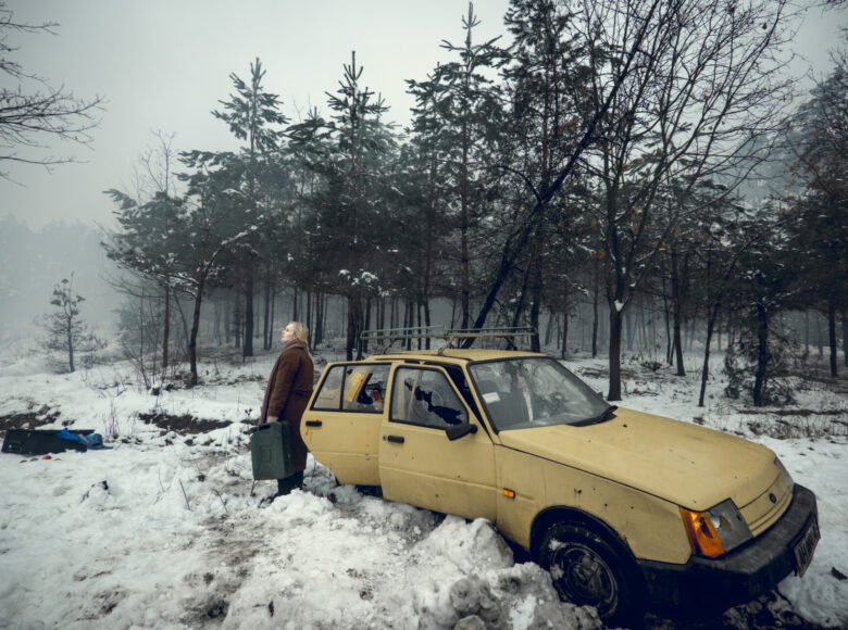 Kadr z filmu. Kobieta stoi w zaśnieżonym lesie, obok zaparkowanego samochodu. W ręku trzyma kanister na benzynę.