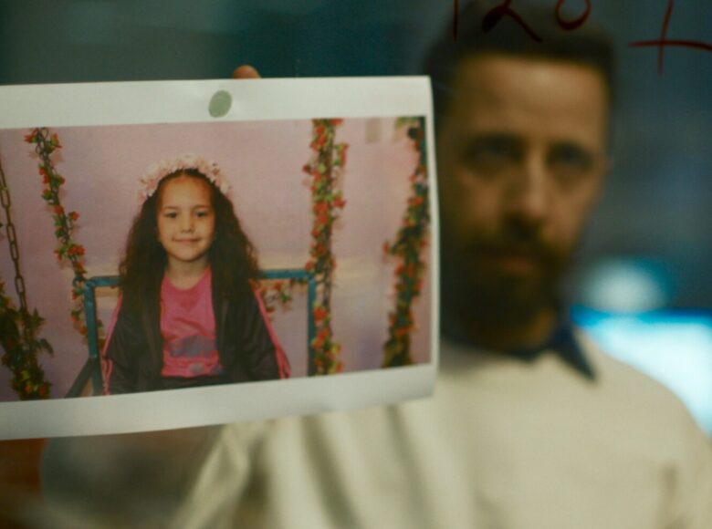 Kadr z filmu. Mężczyzna pokazuje fotografię dziewczynki siedzącej na huśtawce.