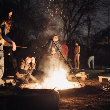 Grupa ludzi wokół ogniska na dworze po zmroku.