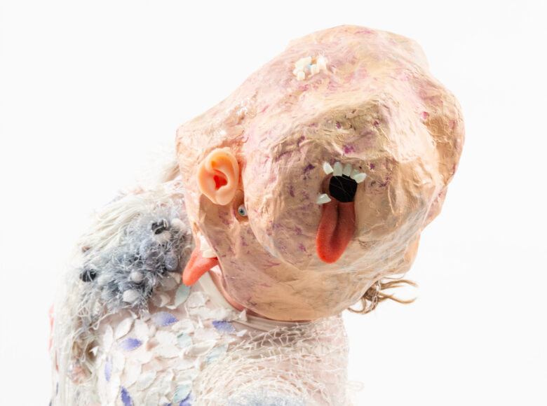 Zbliżenie na osobę w fantazyjnej, teatralnej masce na twarzy. Z tyłu białe tło.